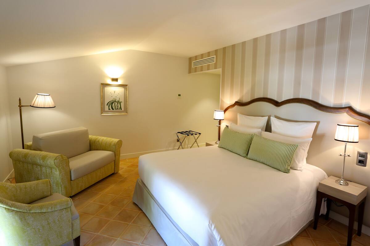 Une chambre d’hôtel avec un grand lit, un canapé, deux lampes, une petite table et un climatiseur fixé au mur.