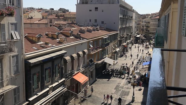 Vista de la calle con edificios, tiendas y terrazas.