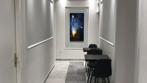 Un pasillo con alfombra estampada, una mesa con sillas y una obra de arte enmarcada en la pared.