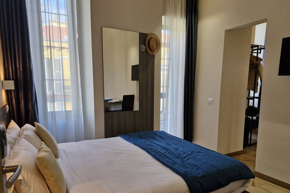 A hotel room with a bed, a desk, and a mirror.