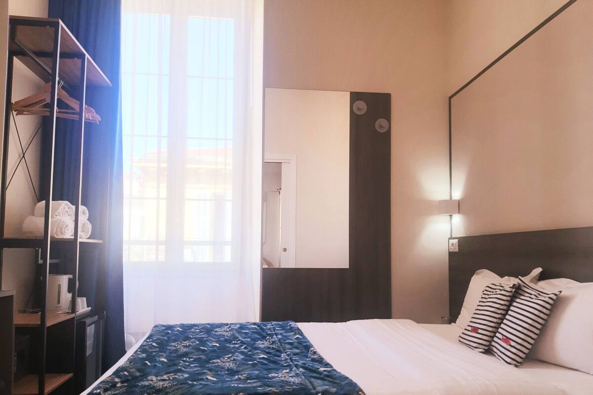 A hotel room with a bed, a wardrobe, a mirror, and a window with curtains.