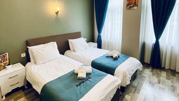 A hotel room with two beds, a nightstand, a wall-mounted lamp, and a window with curtains.
