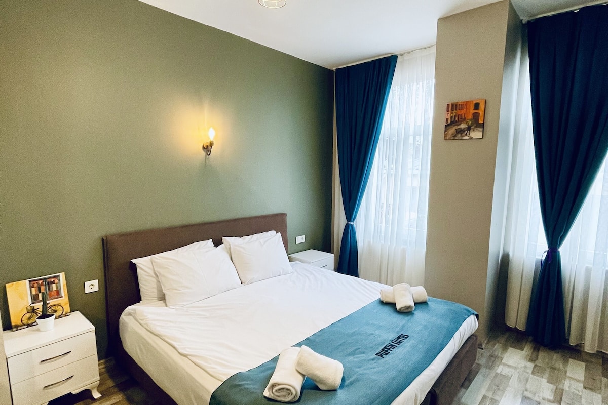 A neatly made bed with a blue bedspread, a bedside table with a lamp, and a picture frame on the nightstand.