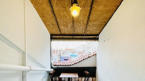 A narrow balcony with a tiled floor, a table with chairs, and a hanging light fixture.