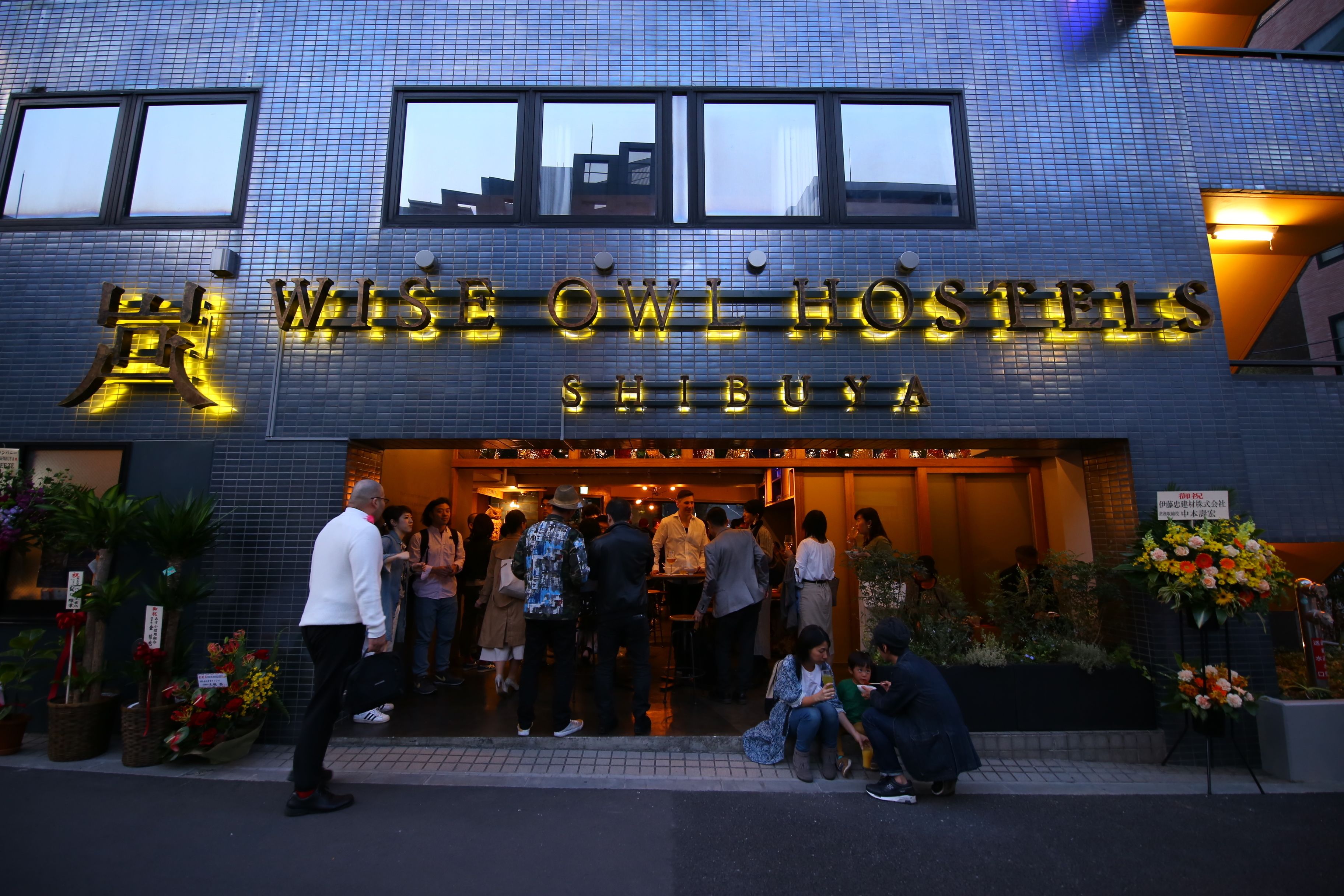 L’extérieur de l’auberge de jeunesse Wise Owl Hostels Shibuya, avec sa façade carrelée et son enseigne lumineuse.