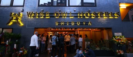 The exterior of Wise Owl Hostels Shibuya with a tiled facade and illuminated signage.