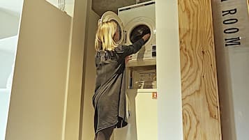 A person operating a front-loading washing machine in a room with a wooden wall and a sign that reads "MUSHROOM".