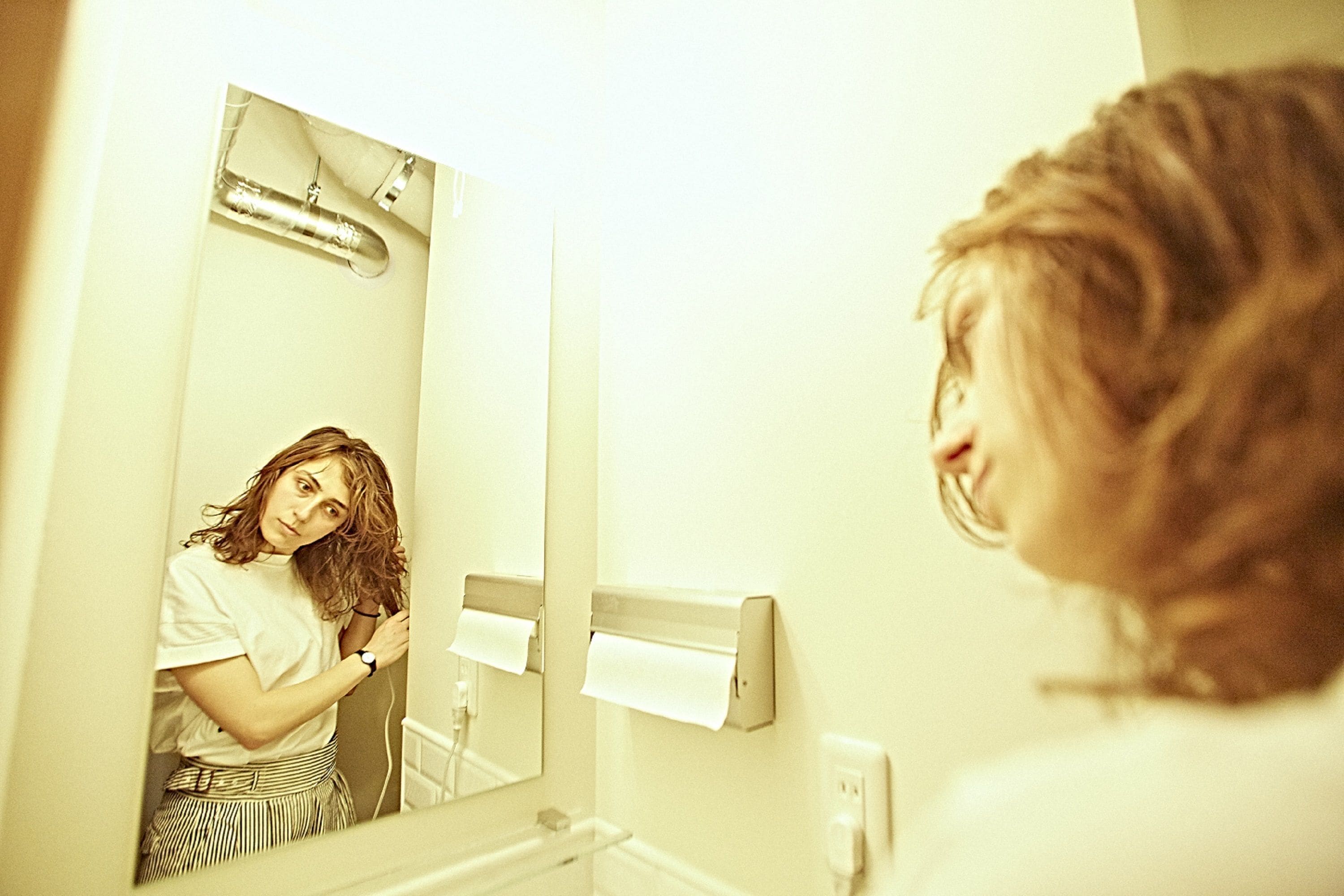 A bathroom with a mirror, a towel dispenser, and a visible pipe above the mirror.