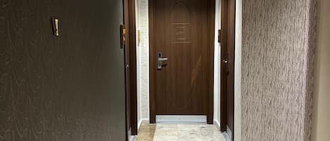 A hallway with a dark patterned wall, a wooden door with a logo, and a tiled floor.