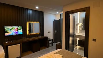 Habitación de hotel moderna con una cama grande, televisor, espejo y baño visible a través de una puerta abierta.