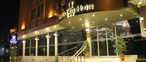 Entrada del Gran Hotel Ezel con señalización iluminada, un juego de escalones y plantas en macetas.