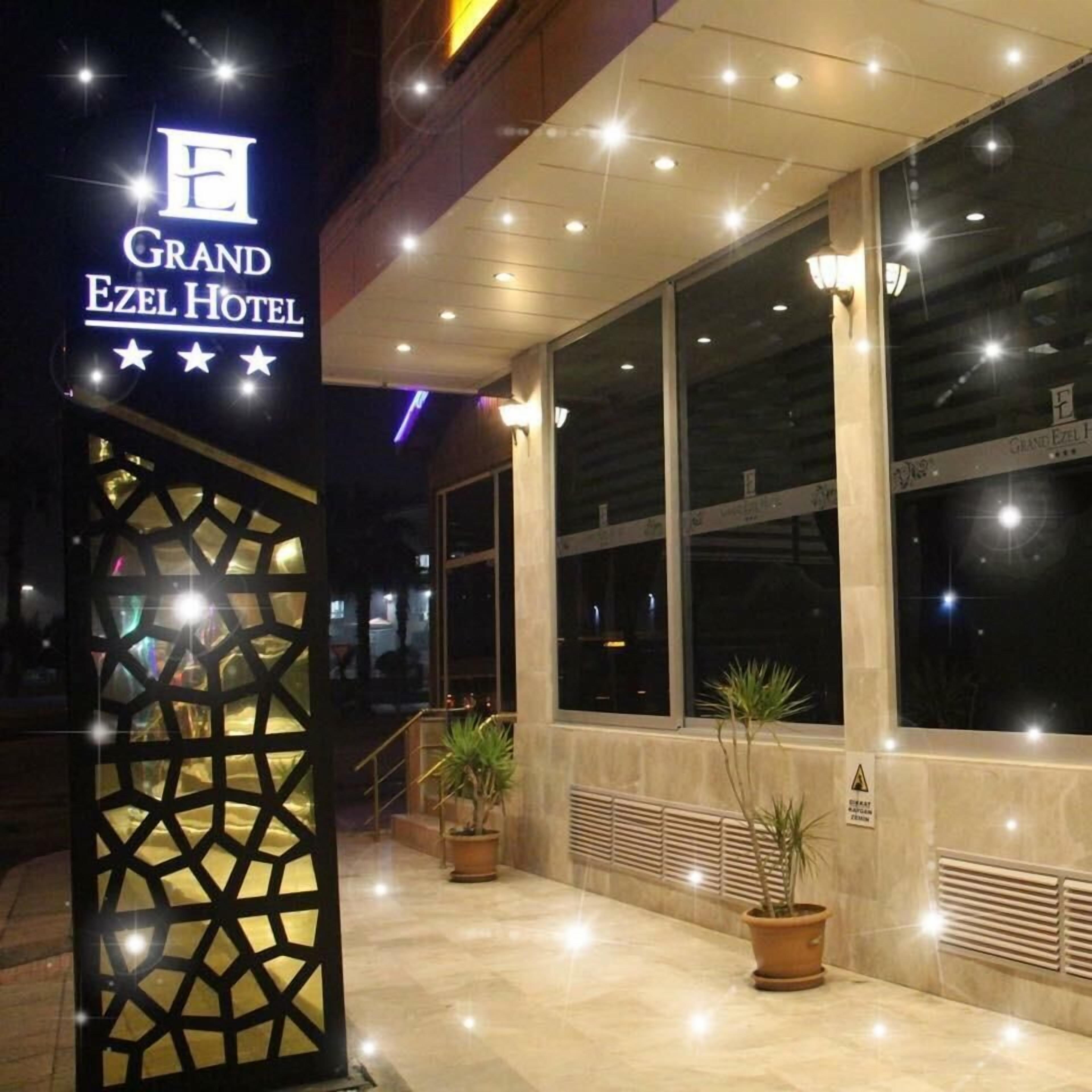 The exterior of the Grand Ezel Hotel with a prominent sign, large windows, and potted plants.