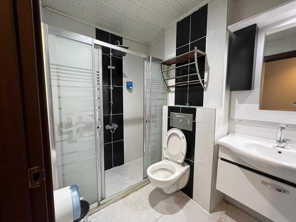 Een moderne badkamer met een douchecabine van glas, een wit toilet en een wastafel met spiegel erboven.