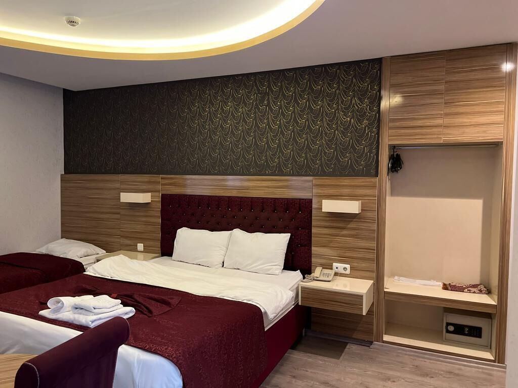 Habitación de hotel con una cama grande, dos mesitas de noche, un armario y un diseño moderno en el techo.