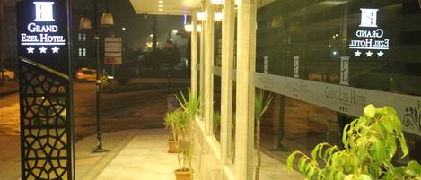 The Grand Ezel Hotel entrance with a sign, potted plants, and a glass facade.