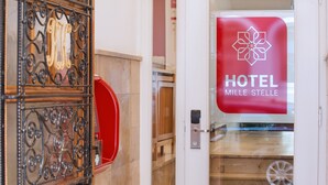 L’entrée d’un hôtel, avec un portail en métal, une boîte aux lettres rouge et une porte en verre ornée du logo de l’hôtel.