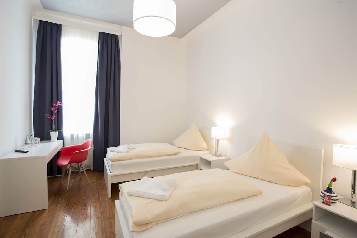 Une chambre d’hôtel avec deux lits, un bureau, une chaise et une lampe.