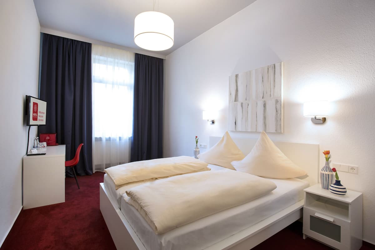 Une chambre d’hôtel équipée d’un lit, d’un bureau, d’une chaise, d’une table de chevet et d’une fenêtre avec des rideaux.