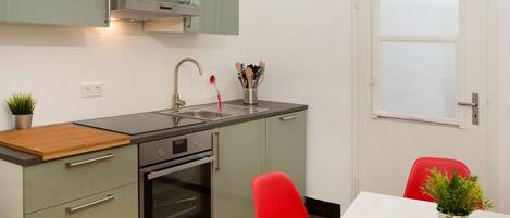 A modern kitchen with a stainless steel sink, a built-in oven, and a red chair.