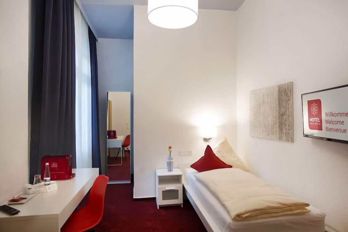 Une chambre d’hôtel comprenant un lit, une table de chevet, une chaise, un bureau et un miroir.