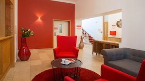 Un hall d’entrée avec un mur rouge, un comptoir d’accueil, un escalier et un canapé gris.