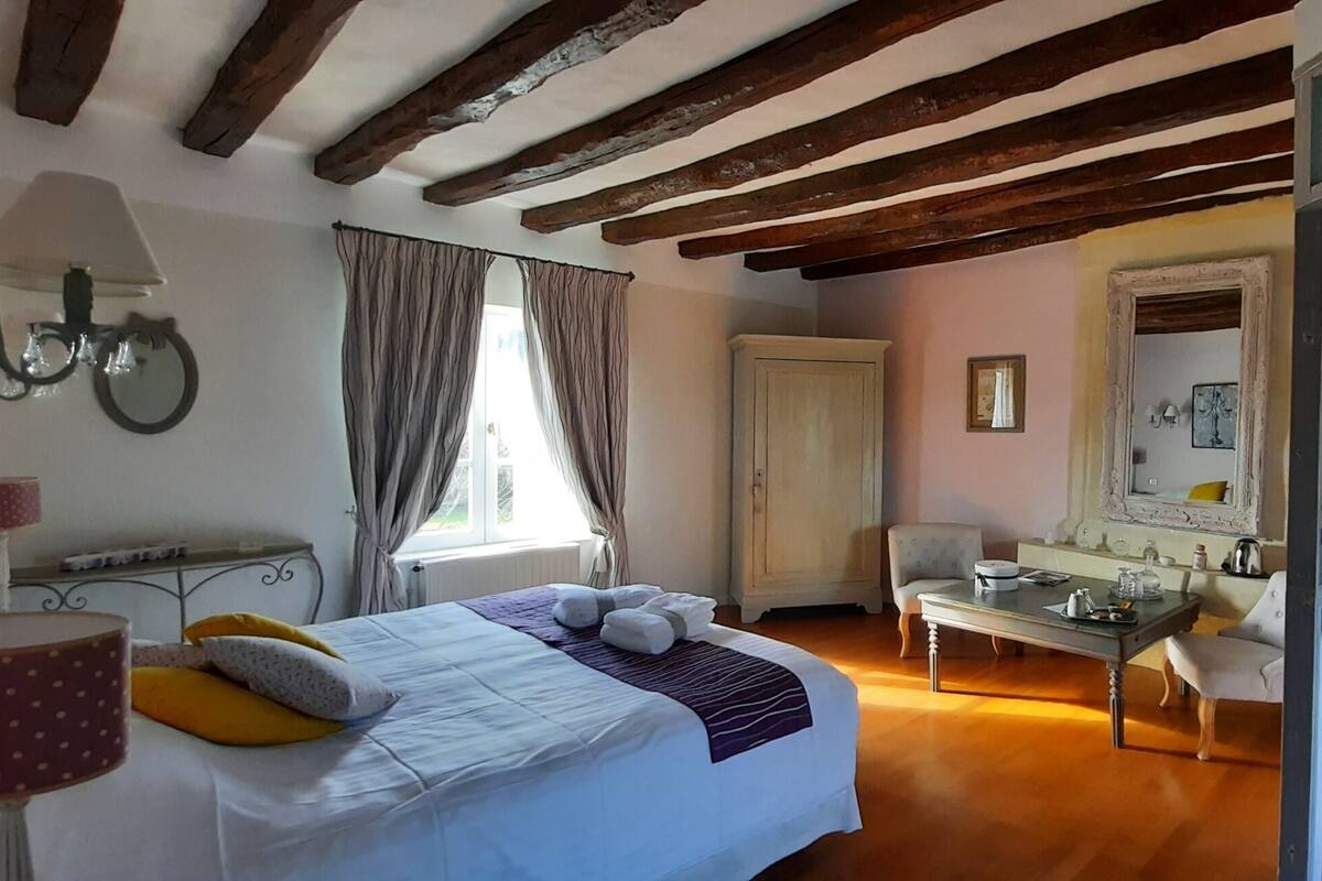 Une chambre à coucher comprenant un lit, une table, une chaise, une armoire et une salle de bain visible à travers une porte ouverte.