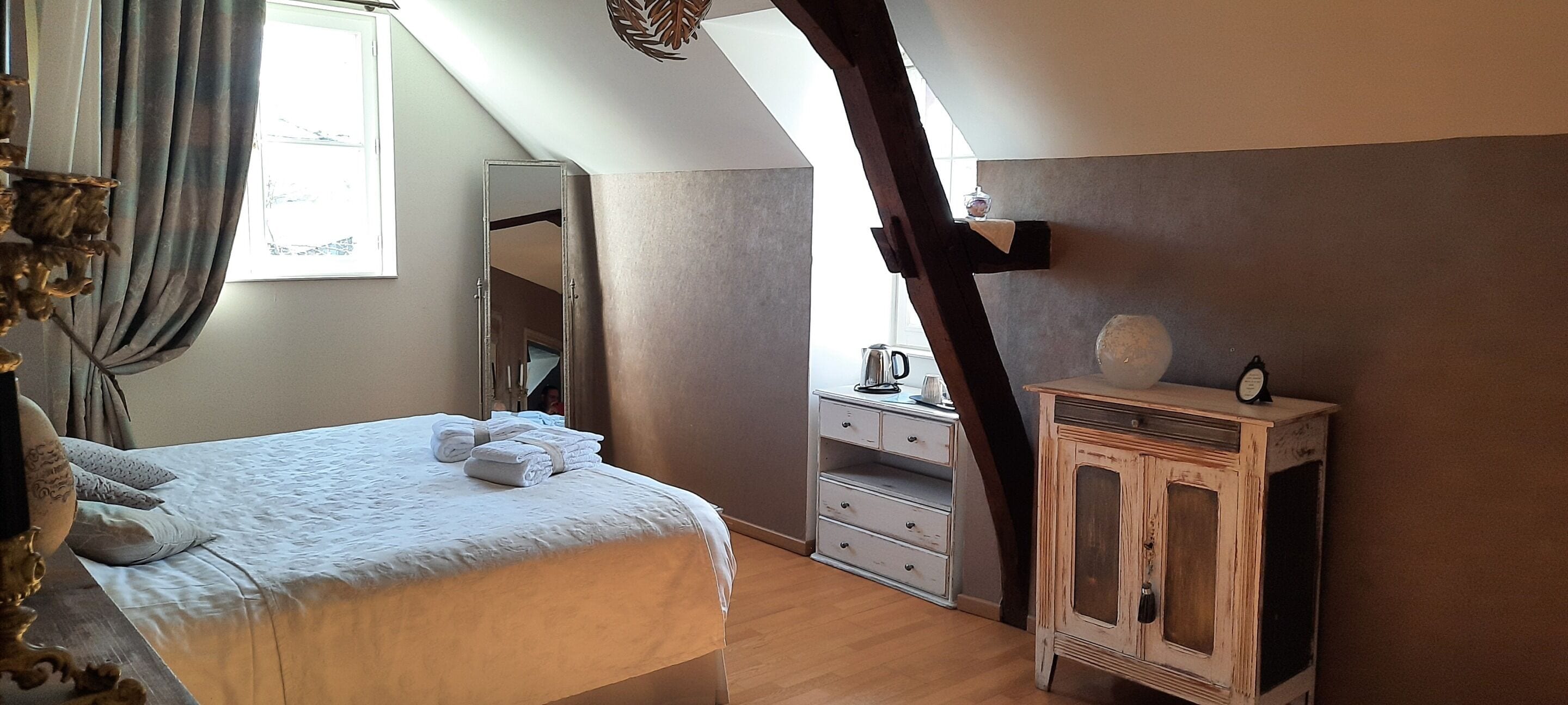 Een slaapkamer met een bed, een dressoir, een spiegel en een raam.