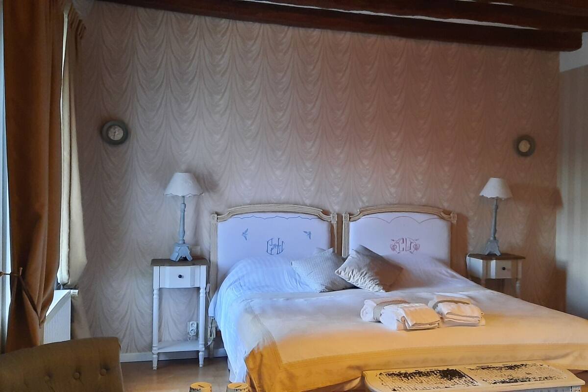 Une chambre à coucher bien aménagée, avec un lit double, deux tables de chevet avec des lampes, une chaise et un présentoir à photos fixé au mur.