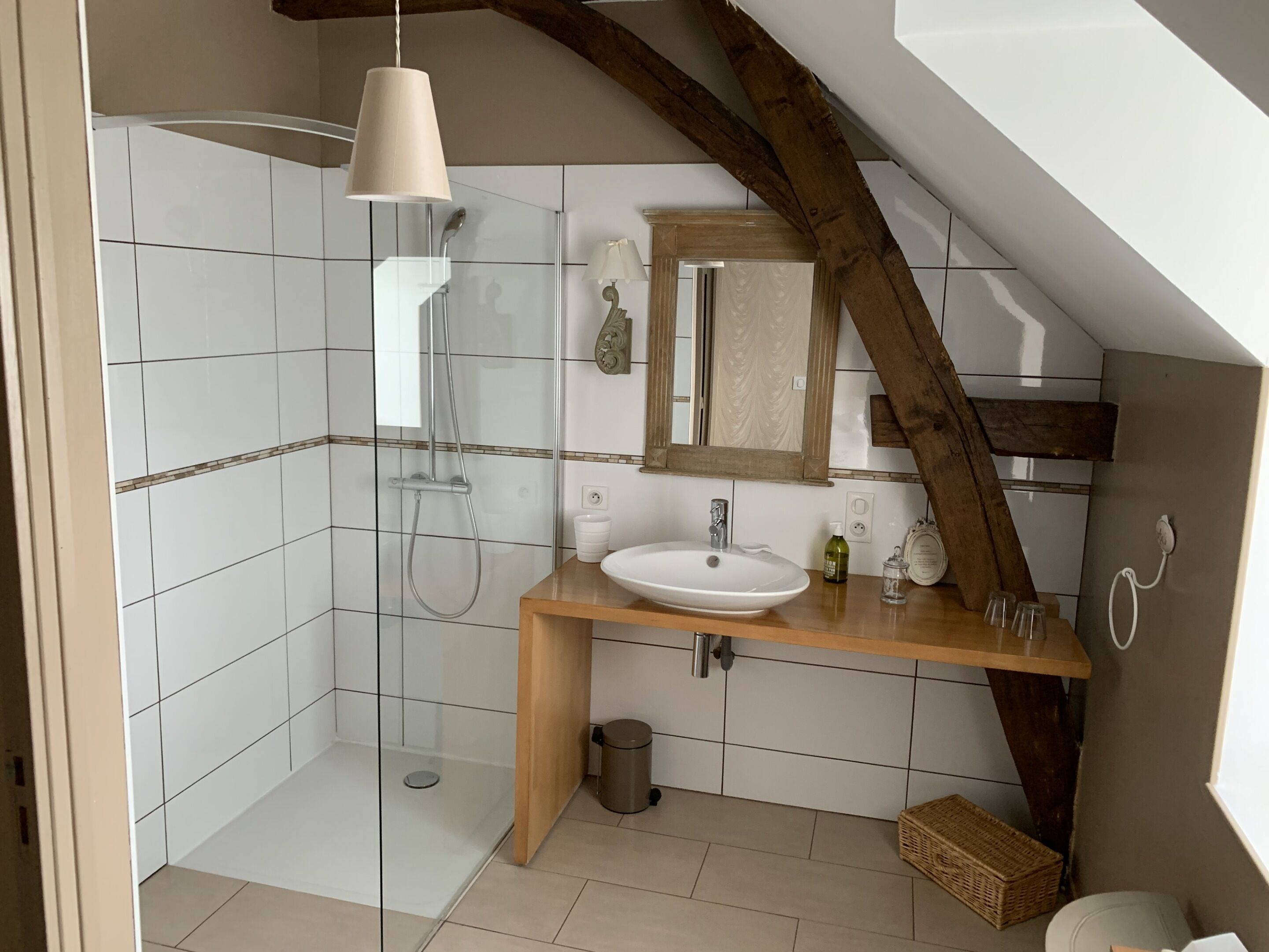 Un baño moderno con ducha envuelta en vidrio, tocador de madera y un espejo grande.