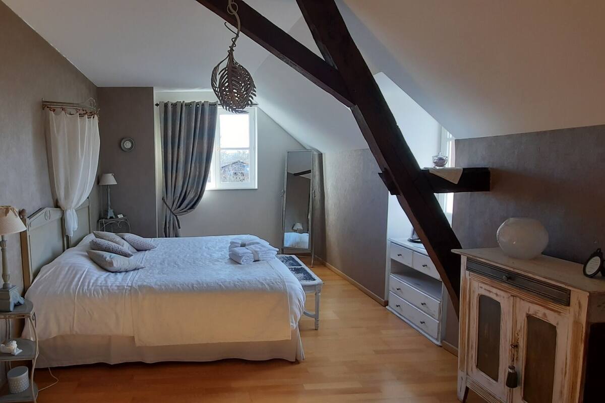 Une chambre à coucher avec un grand lit, une commode, un miroir et une fenêtre avec des rideaux.