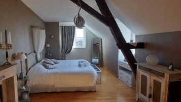 A bedroom with a large bed, a dresser, a mirror, and a window with curtains.