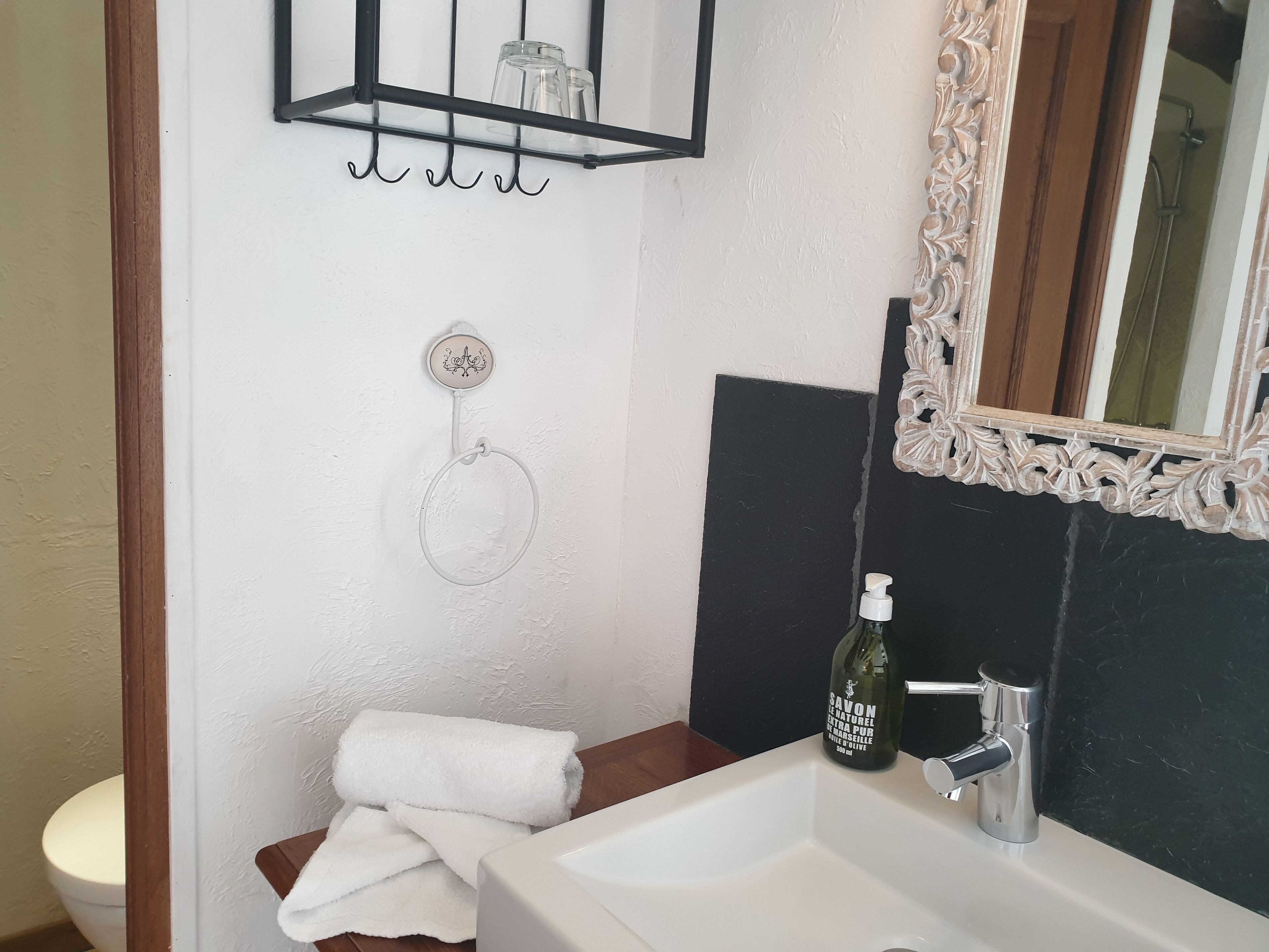 Un baño con un lavabo blanco, un espejo con marco decorativo, una botella de jabón y una toalla sobre el mostrador.