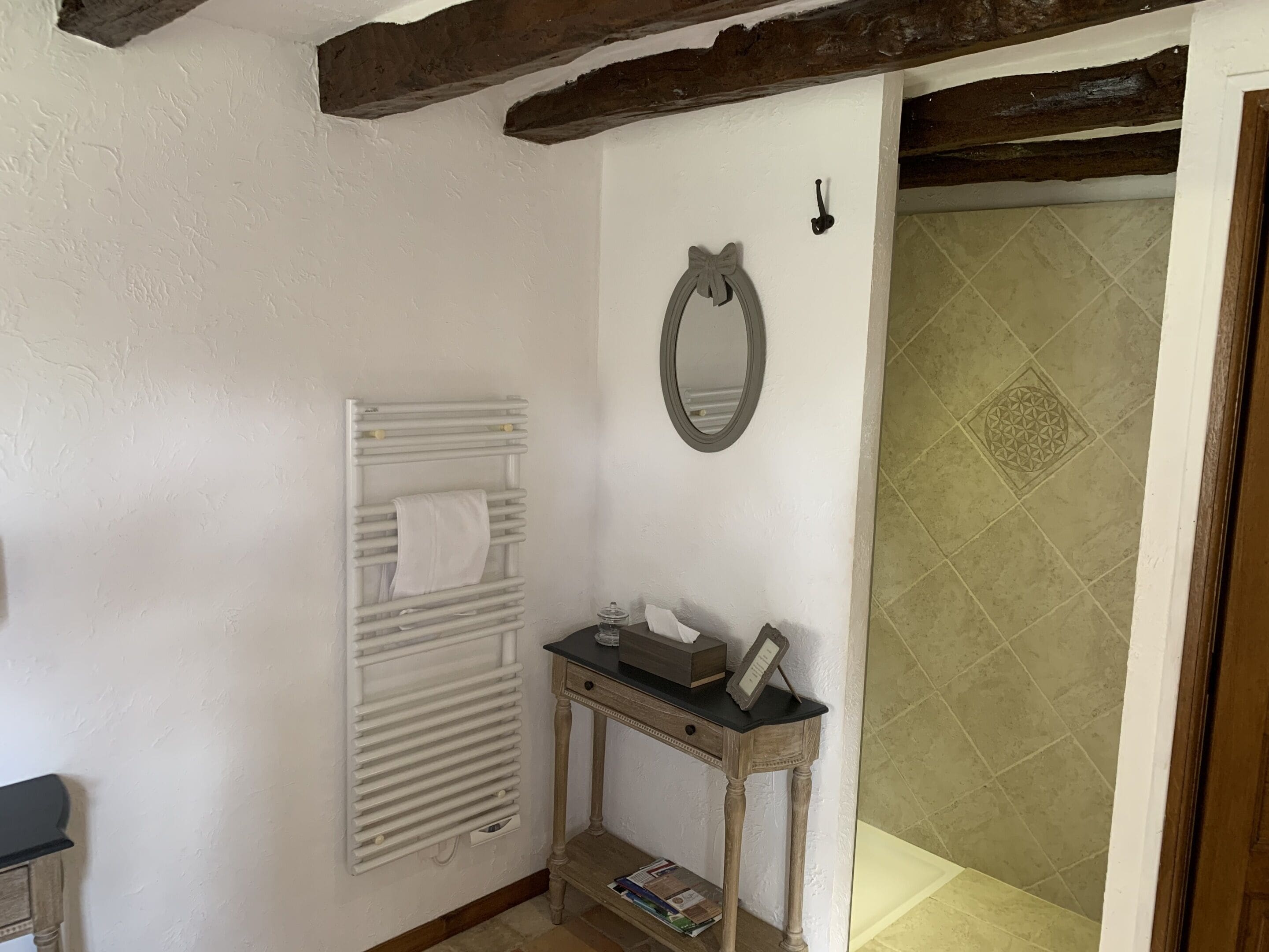 Een badkamer met een witte radiator, een spiegel, en een klein tafeltje met een zakdoosje en een ingelijste foto.