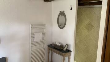 Een badkamer met een witte radiator, een spiegel, en een klein tafeltje met een zakdoosje en een ingelijste foto.