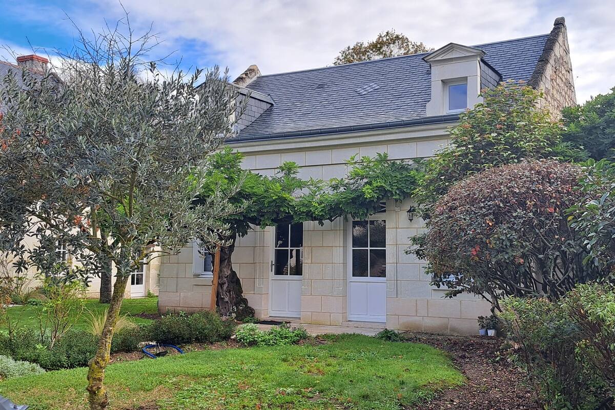 Une maison à deux étages avec une façade en pierre, un jardin bien entretenu et un ciel dégagé.