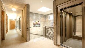 A modern hallway with a wooden floor, a glass elevator, and a concrete wall with a decorative panel. - Le Kube Annecy Appartements De Luxe (Annecy)