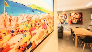A large painting of a crowded beach scene, a wooden dining table, and modern art on the wall. - Le Kube Annecy Appartements De Luxe (Annecy)