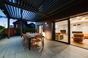 An outdoor dining area with a table and chairs, a pergola, and a view of a house in the background.