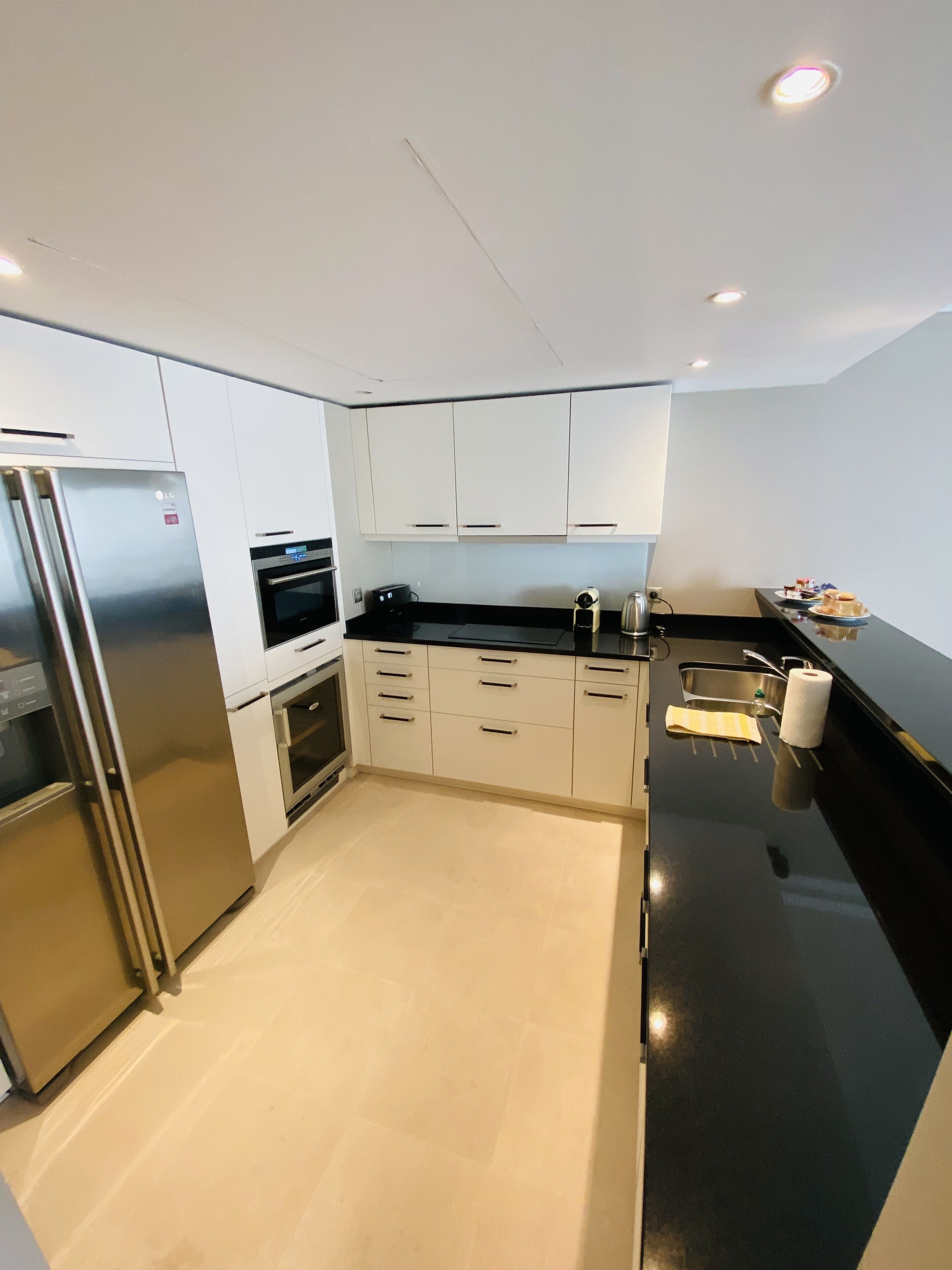 A modern kitchen with white cabinets, a stainless steel refrigerator, a built-in oven, and a black countertop.