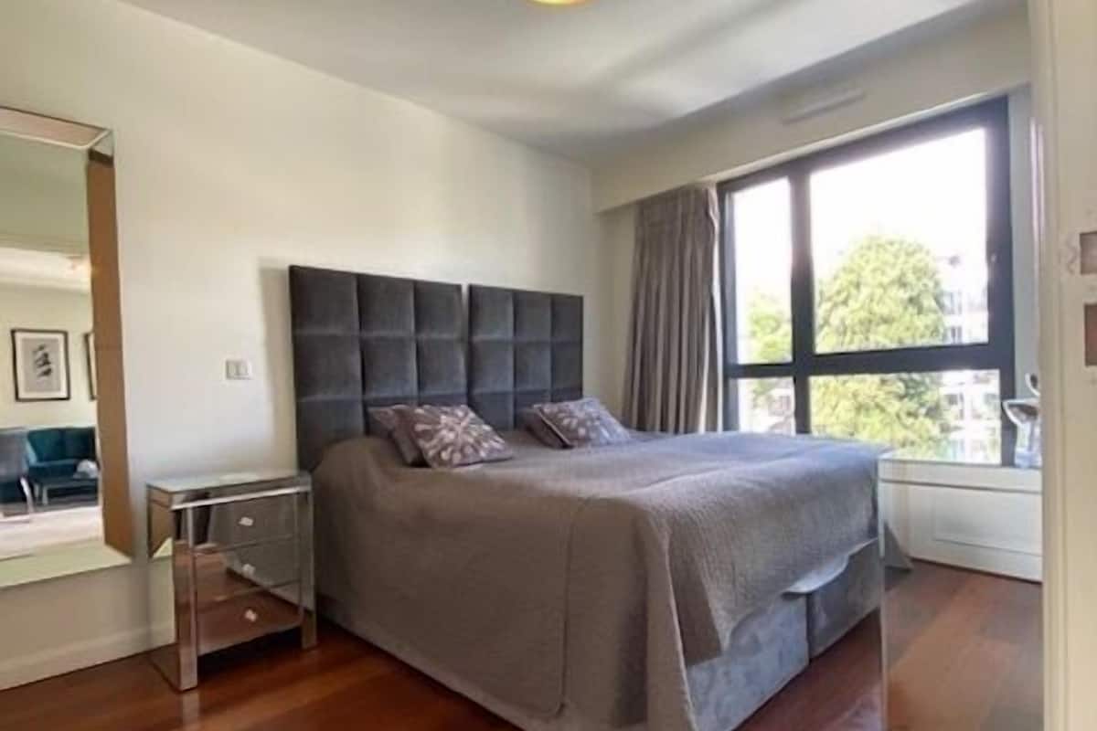 Un dormitorio moderno con una cama grande, una mesita de noche y un ventanal con cortinas.