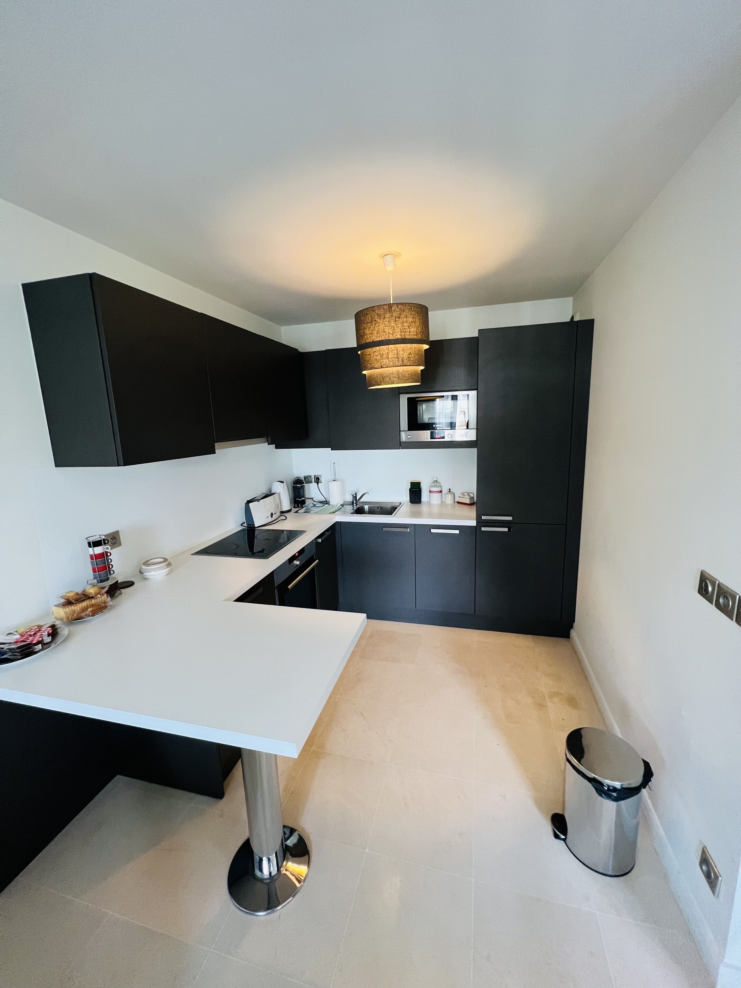 Une cuisine moderne avec des meubles de couleur noire, un plan de travail blanc, un évier en acier inoxydable et un luminaire suspendu.
