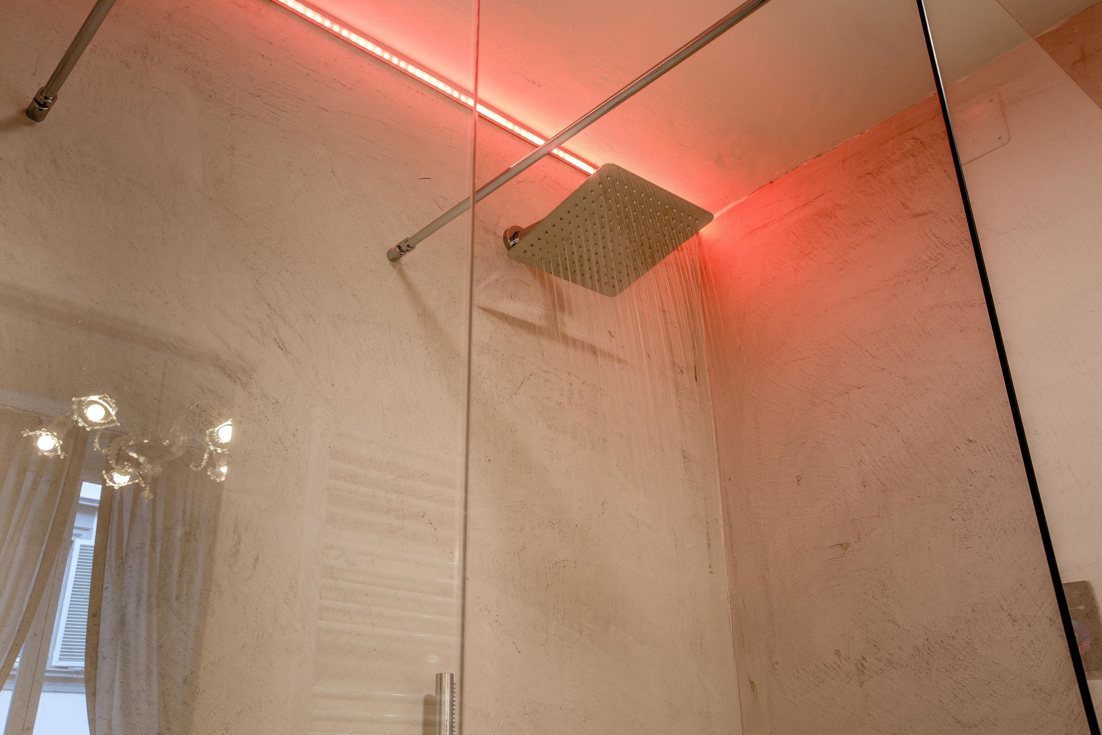 A modern shower with a square head, a visible water stream, and a red LED light strip above.