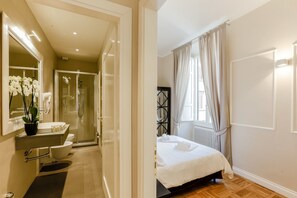 A modern hotel room with a bathroom, a shower, a bed, and a window with curtains. - Relais Tosinghi (Florence)