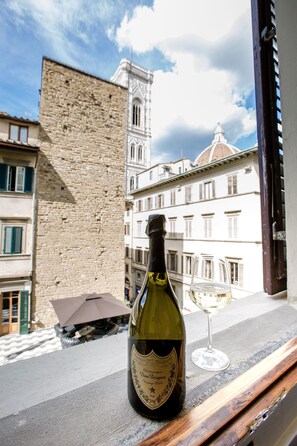 A bottle of wine and a glass on a balcony with a view of historic buildings and a tower. - Relais Tosinghi (Florence)