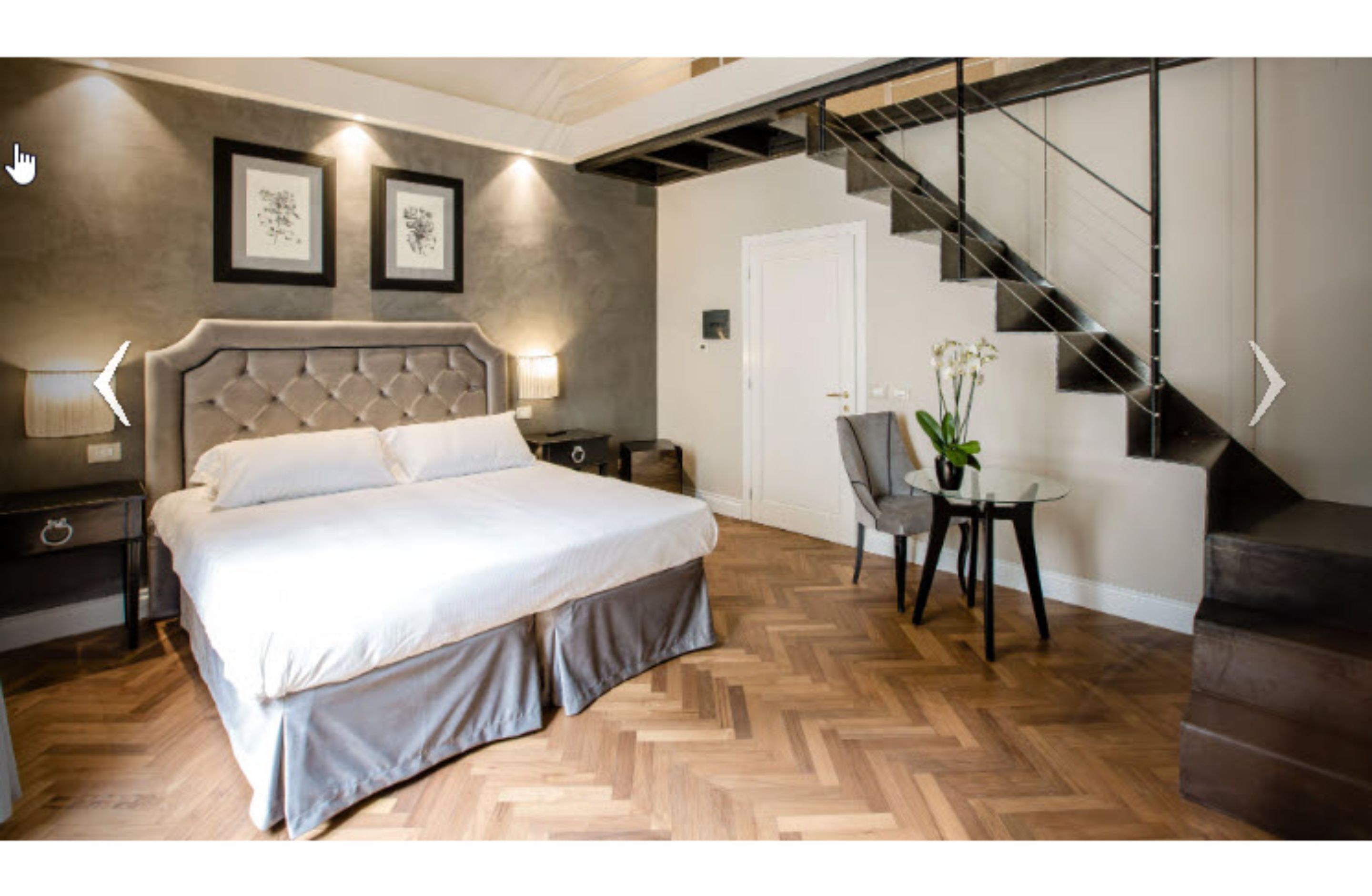 A bedroom with a bed, a nightstand, a chair, a table with a plant, and a staircase.