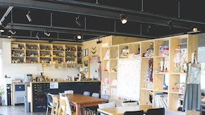 Un café amplio con mesas y sillas de madera, un menú en pizarra y estantes con diversos artículos.