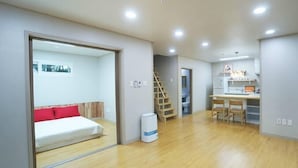 Una habitación de hotel moderna con piso de madera, cama con almohadas rojas, escritorio con dos sillas y una escalera que conduce a otra habitación.