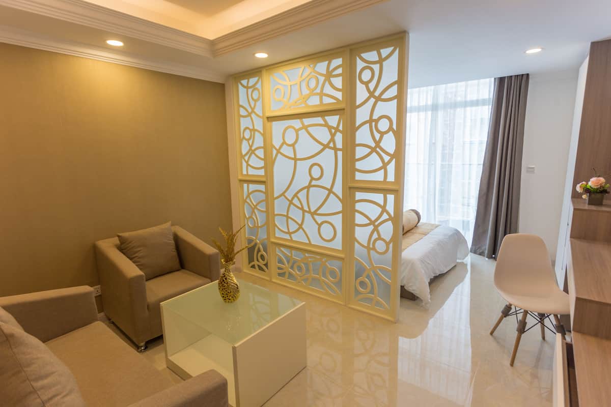 Ein modernes Hotelzimmer mit einer Couch, einem Glastisch, einem dekorativen Raumteiler, einem Bett und einem Schreibtisch.