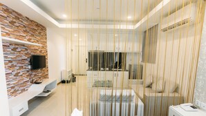 Ein modernes Hotelzimmer mit Ziegelwand, Flachbildfernseher, Bett, Nachttisch und einem kleinen Beistelltischchen mit Telefon.