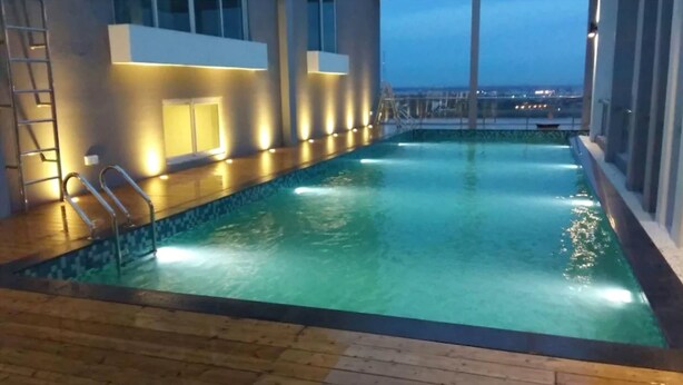 Ein Innenpool mit Holzterrasse, Metallgeländern und Blick auf die städtische Silhouette im Abendlicht.